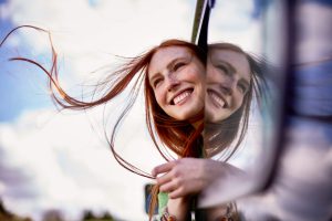 Mulher ruiva sorridente com a cabeça para fora da janela do carro.