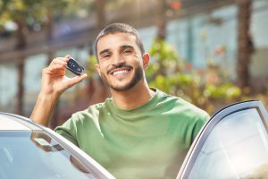 homem-de-blusa-verde-sorrindo-na-porta-de-carro-com-chave-na-mao