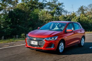 Chevrolet Onix Premier vermelho em movimento na estrada, com rodas de liga leve e detalhes cromados em destaque, durante o dia