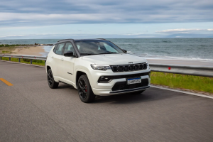 Jeep Compass branco em movimento na estrada costeira, com vista para o mar ao fundo em um dia ensolarado