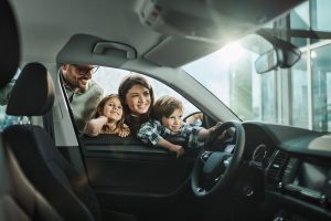 Homem branco com mulher e dois filhos olhando interior de carro em concessionária