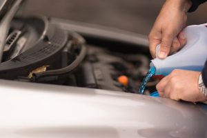 Pessoa colocando líquido de arrefecimento azul no reservatório do motor, com o capô do carro aberto