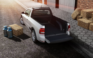 Volkswagen Saveiro branca estacionada em ambiente rural, caçamba aberta em destaque, cercada por galões de leite e palha espalhada ao redor.