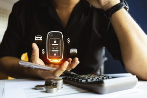 Man analyzing car-related expenses with calculator, coins, and digital car key icon, representing financial planning, budgeting, and vehicle costs.