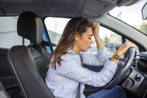 mulher dentro do carro, apoiando a cabeça no volante com expressão de frustração, porque o veículo não dá partida devido a um defeito.