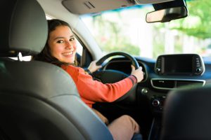 happy-teen-girl-smiling-and-enjoying-driving-a-car-from-the-drivers-seat-poses-for-a-portrait