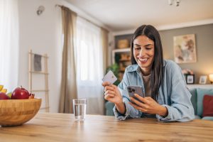 a-young-cheerful-woman-using-her-smartphone-to-shop-online-and-holding-a-credit-card