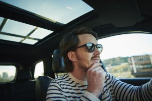 Pessoa usando óculos escuros dirigindo carro seminovo com teto solar aberto, aproveitando a iluminação natural