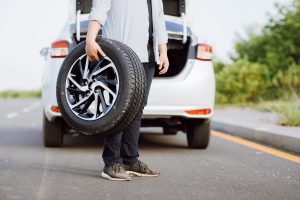 Handsome Asian young man holding spare wheel against for changing flat tire on the road.