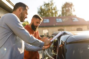 Copy space shot of mid adult man selling his old car and giving customer a clipboard to sign after he purchased it.