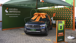 carro seminovo na saída da loja da Localiza, com um laço laranja sobre o capô, simbolizando a conquista e a entrega do veículo ao novo proprietário.