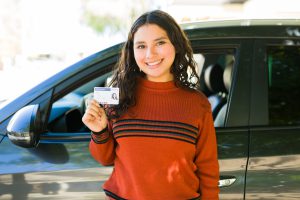 happy-teenager-posing-with-her-drivers-license-next-to-her-new-car-outside
