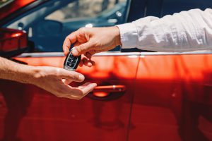 dealer-giving-car-keys-to-the-new-owner-close-up-of-hands-on-the-background-of-red-automobile