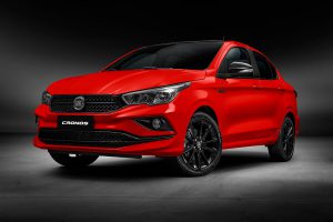 Carro Fiat Cronos vermelho fotografado em estúdio com foco na parte dianteira. A iluminação destaca a grade frontal, os faróis e as linhas do capô, com fundo neutro e uniforme.