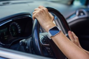 close-upofhandsholdingsteeringwheelinsidemoderncarwith