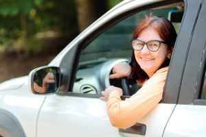 Mulher madura sorrindo no banco do motorista do seu carro.