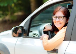 Mulher madura sorrindo no banco do motorista do seu carro.