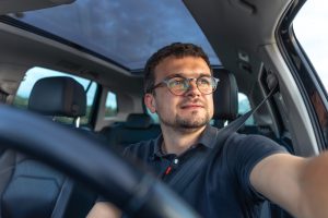Homem dirigindo um carro, olhando para o lado com expressão positiva durante o dia.