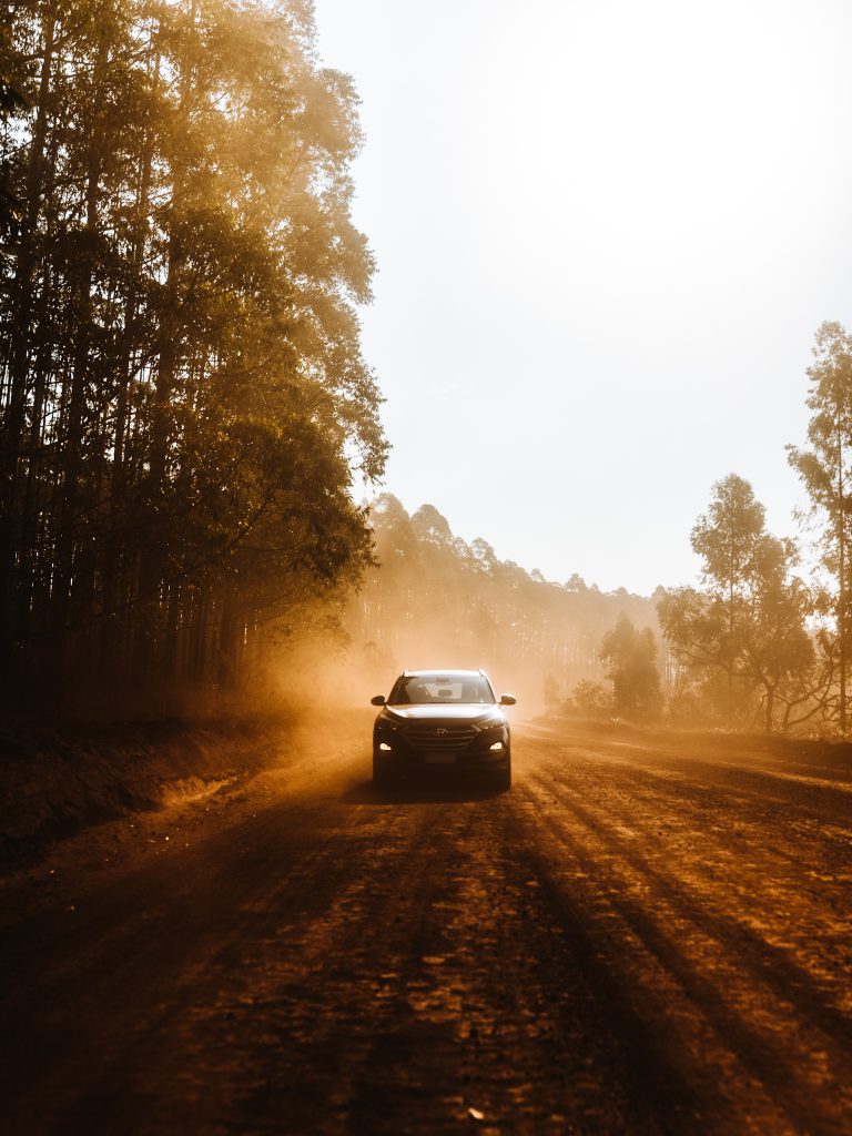 Vista frontal do New Tucson, um carro robusto com faróis angulosos andando sobre uma estrada de terra com árvores compridas nas margens