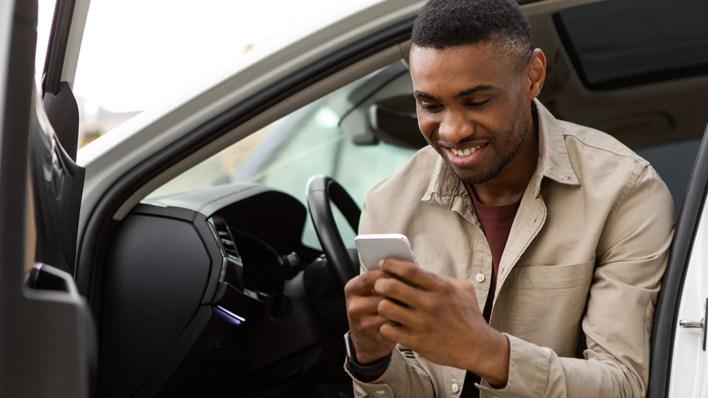 Homem sentado no carro, com a porta aberta, confere no celular a pontuação da CNH.