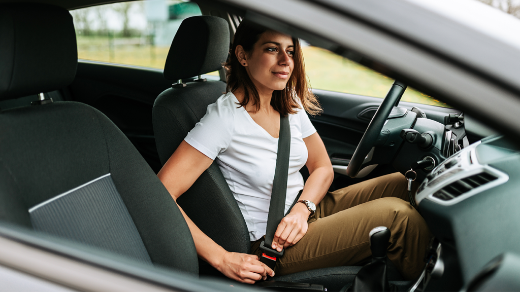 Dentro do carro, mulher coloca o cinto de segurança.