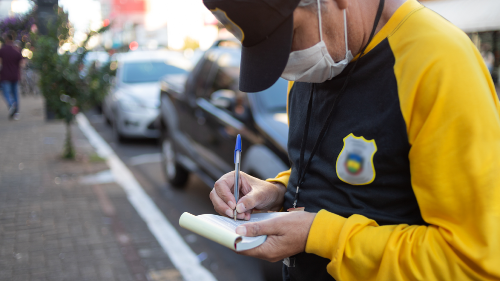 Oficial é visto anotando informações sobre o carro para aplicação de multa de trânsito.