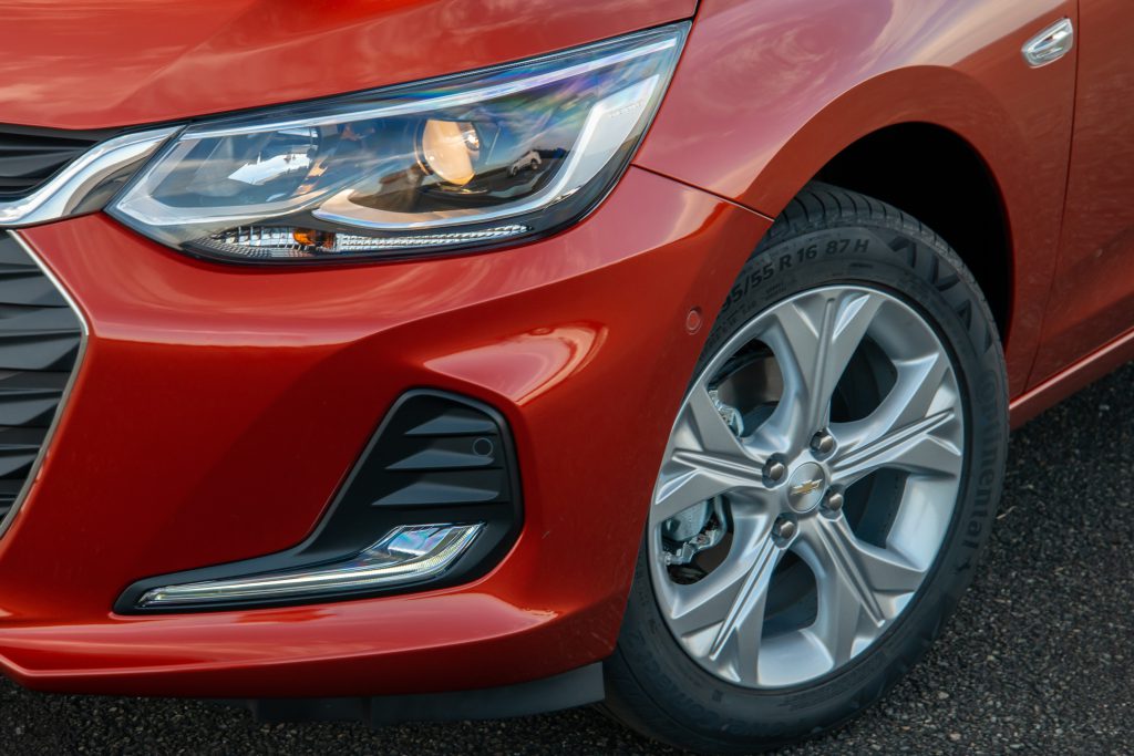 Farol do Chevrolet Onix vermelho em destaque, com design afilado e acabamento moderno que reforça a identidade visual do hatch.