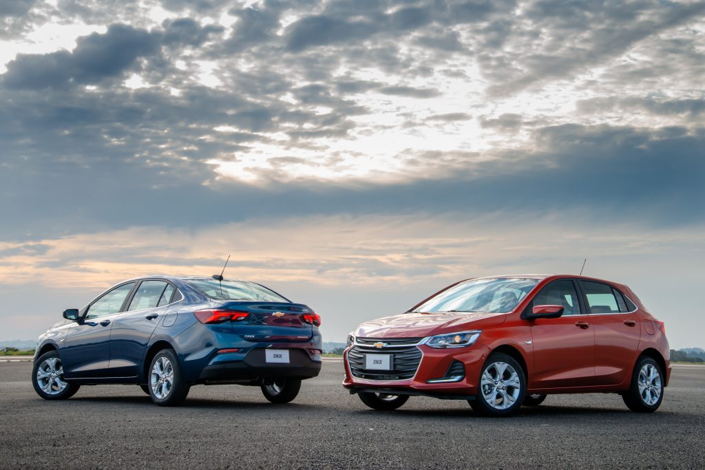 Chevrolet Onix azul e vermelho estacionados lado a lado, evidenciando as diferentes cores e o design marcante do hatch compacto.