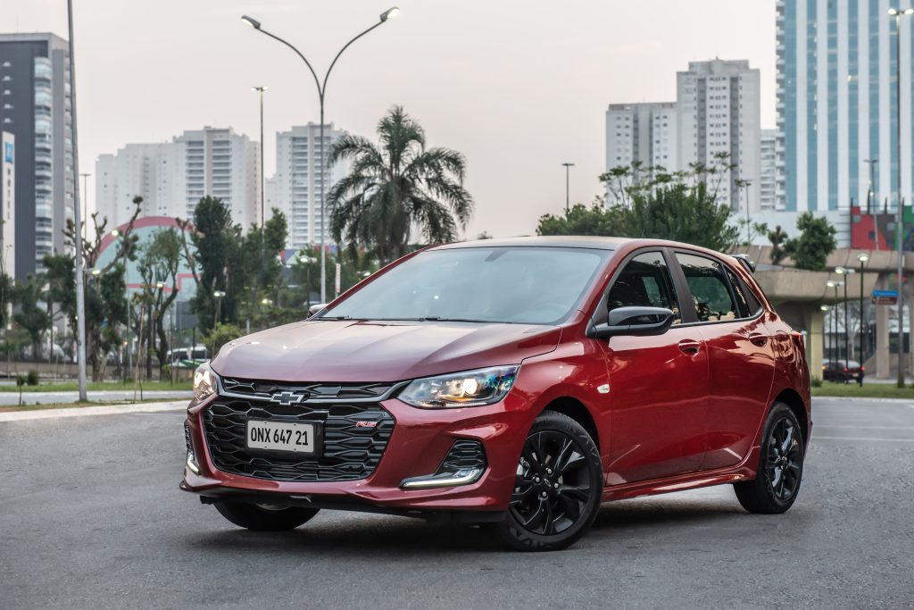 Chevrolet Onix vermelho em movimento na pista, com rodas em destaque e paisagem urbana ao fundo, transmitindo agilidade e dinamismo.