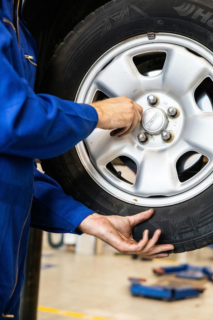 Homem observa de perto o pneu de um carro, avaliando possíveis desgastes ou a necessidade de alinhamento e balanceamento.