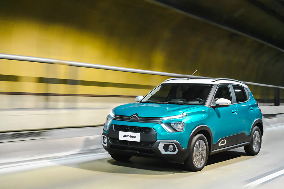 Citroën C3 azul em movimento por avenida, destacando design moderno e linhas aerodinâmicas.