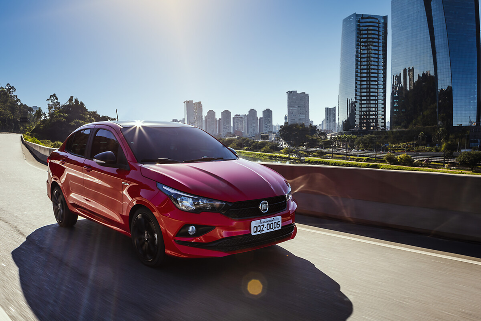 Fiat Cronos vermelho em movimento em uma estrada, visto de ângulo lateral, com paisagem ao fundo.