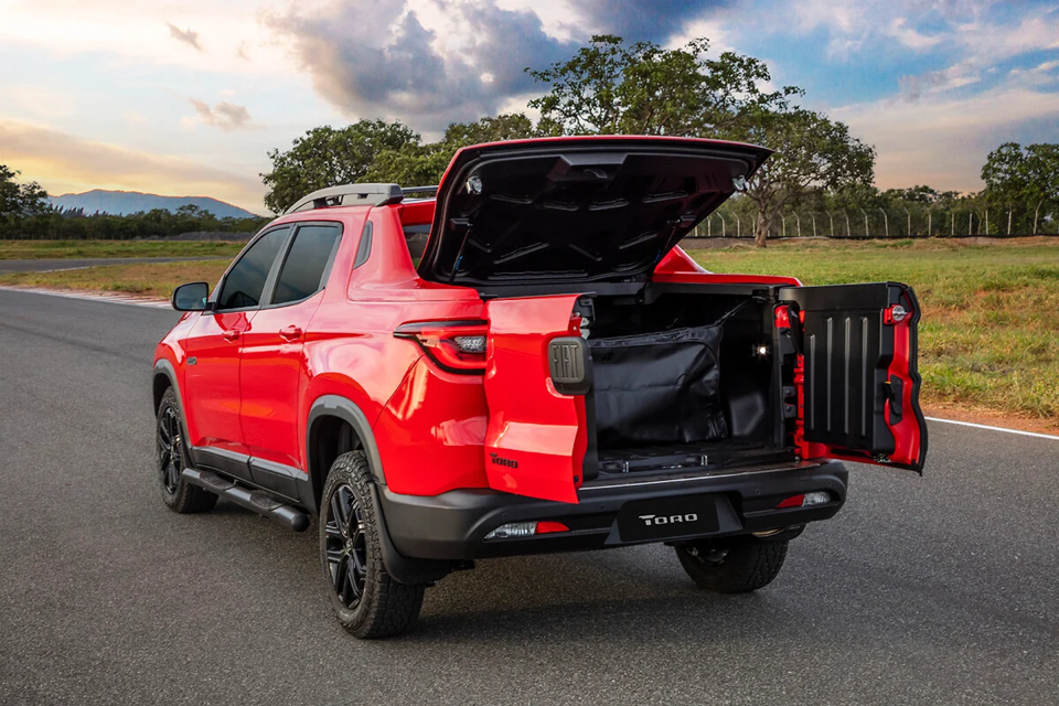Fiat Toro vermelha com o porta-malas aberto, destacando a caçamba ampla e funcional da picape em ambiente externo.
