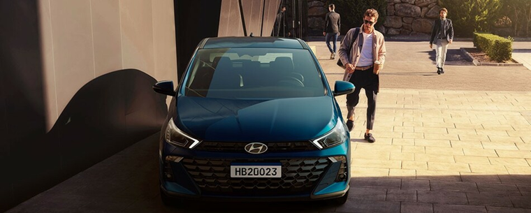 Homem se aproximando de um Hyundai HB20 azul estacionado, em cenário urbano, transmitindo sensação de praticidade e uso no dia a dia.