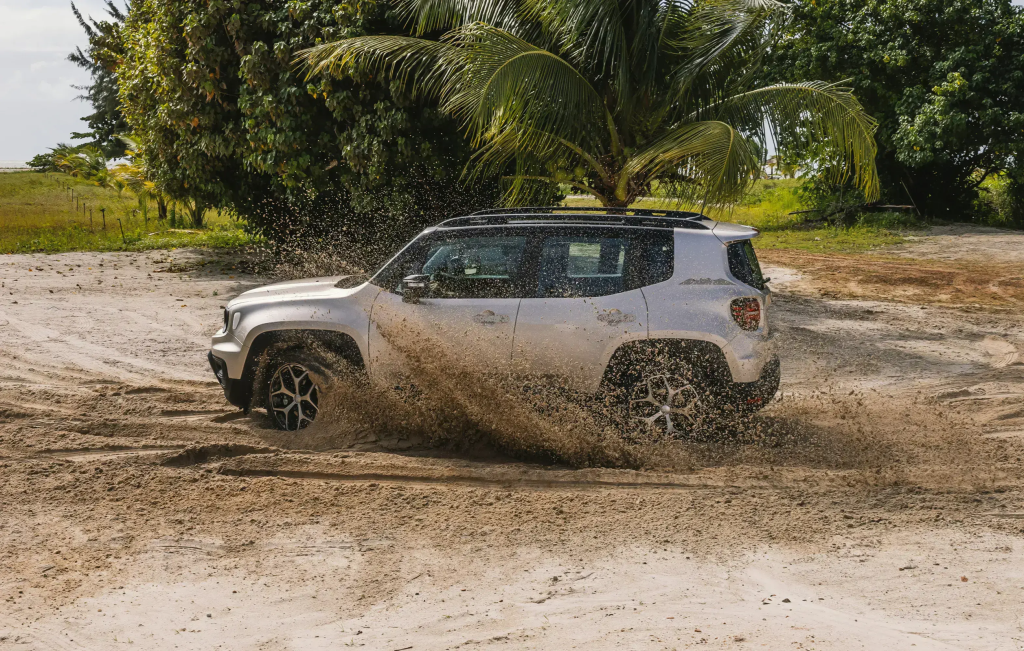 Jeep Renegade cinza em movimento, levantando lama ao atravessar terreno molhado.