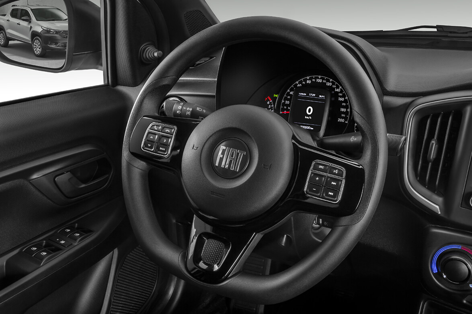 Painel da Fiat Strada visto do interior, com volante, central multimídia e comandos de ar-condicionado em destaque