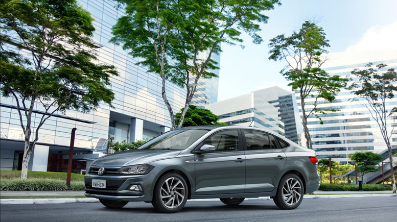 Volkswagen Virtus cinza em movimento em uma avenida urbana, com prédios ao fundo e luzes da cidade refletindo na carroceria."