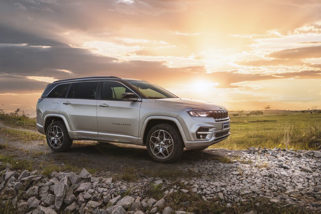 Jeep Commander estacionado ao pôr do sol em um cenário montanhoso, com pedras espalhadas pelo chão.