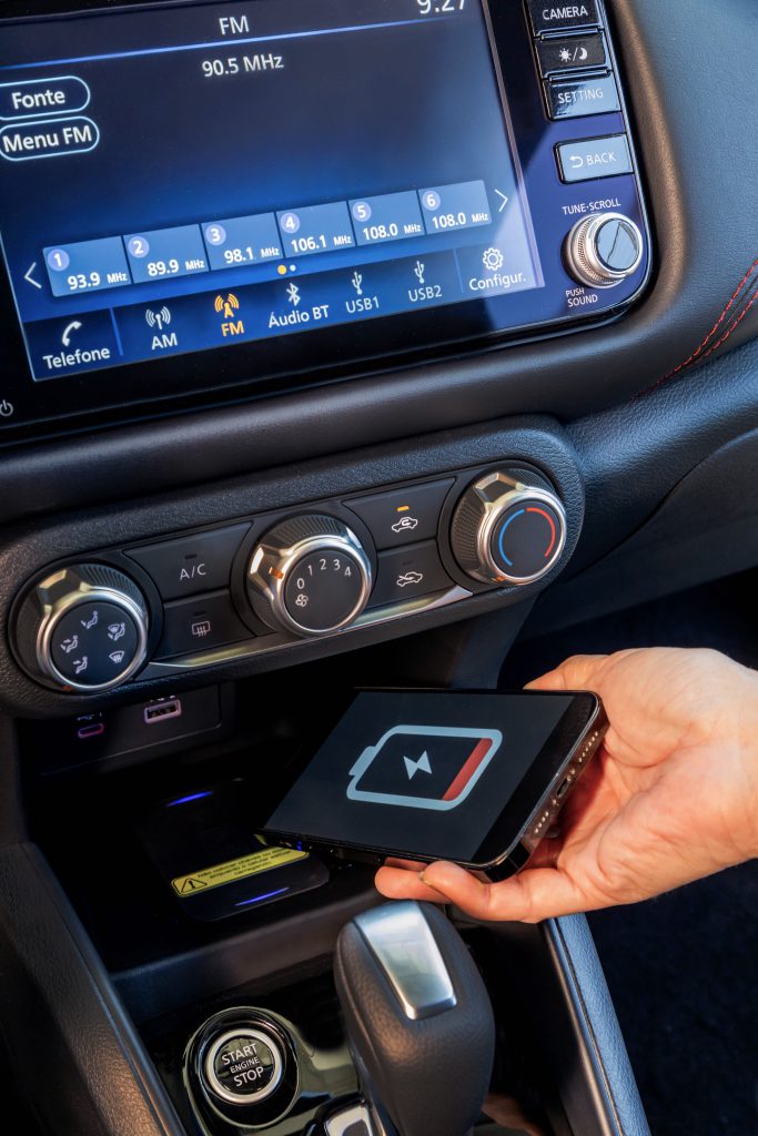 Mão segurando um celular dentro do Nissan Kicks, mostrando o carregamento por indução no console central.