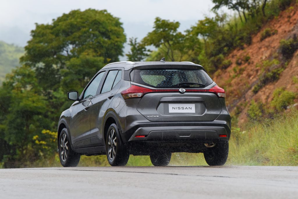 Nissan Kicks Sense cinza visto pela traseira em movimento na estrada.
