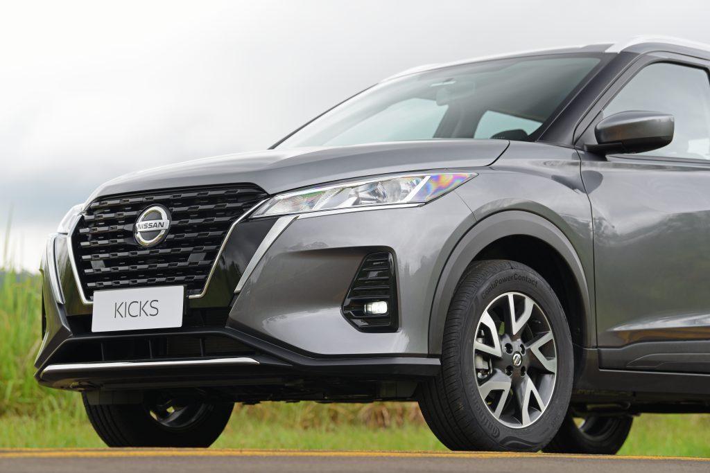 Nissan Kicks visto de frente, com foco na grade frontal e nos faróis, em destaque no ambiente externo."