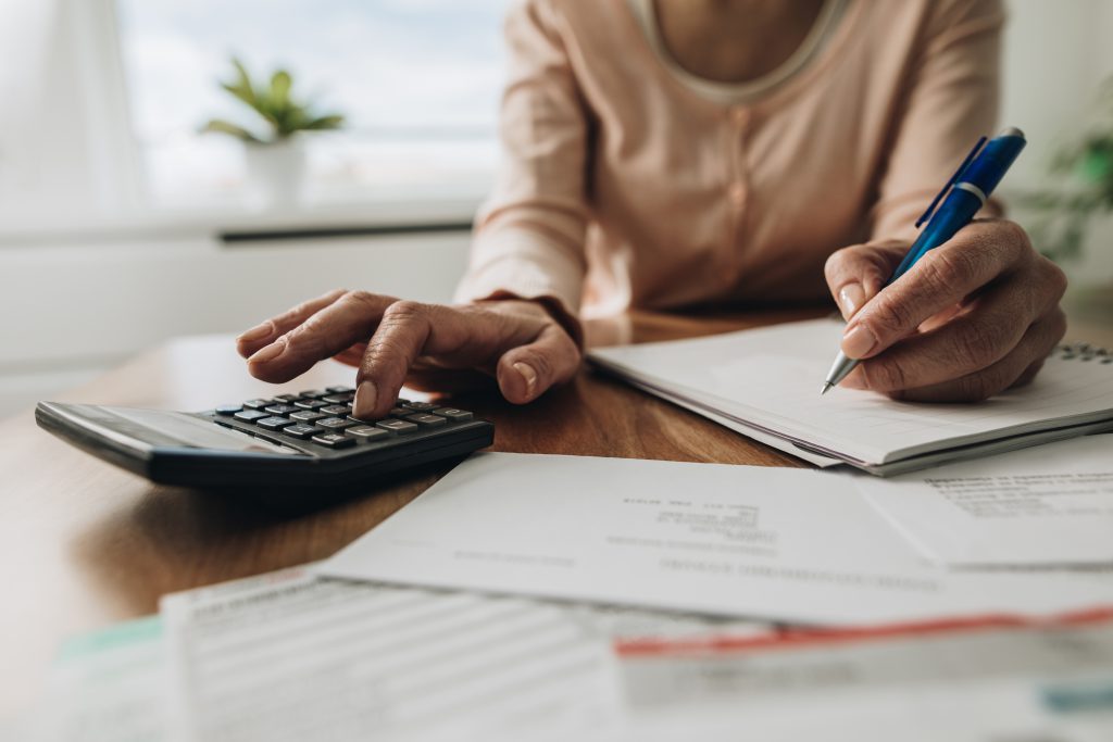 pessoa com calculadora e caneta na mão, fazendo contas para calcular o financiamento de um carro seminovo.