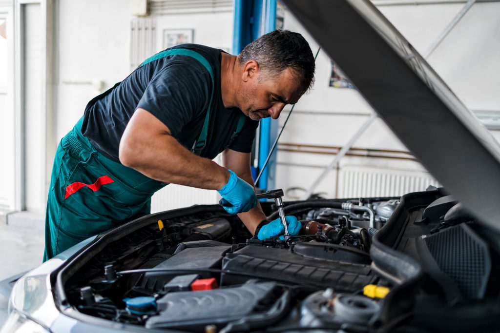 Mecânico inspecionando o motor de um carro com o capô aberto em uma oficina
