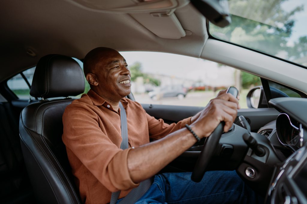 Homem dirigindo o carro a caminho do trabalho, com as mãos firmes no volante.