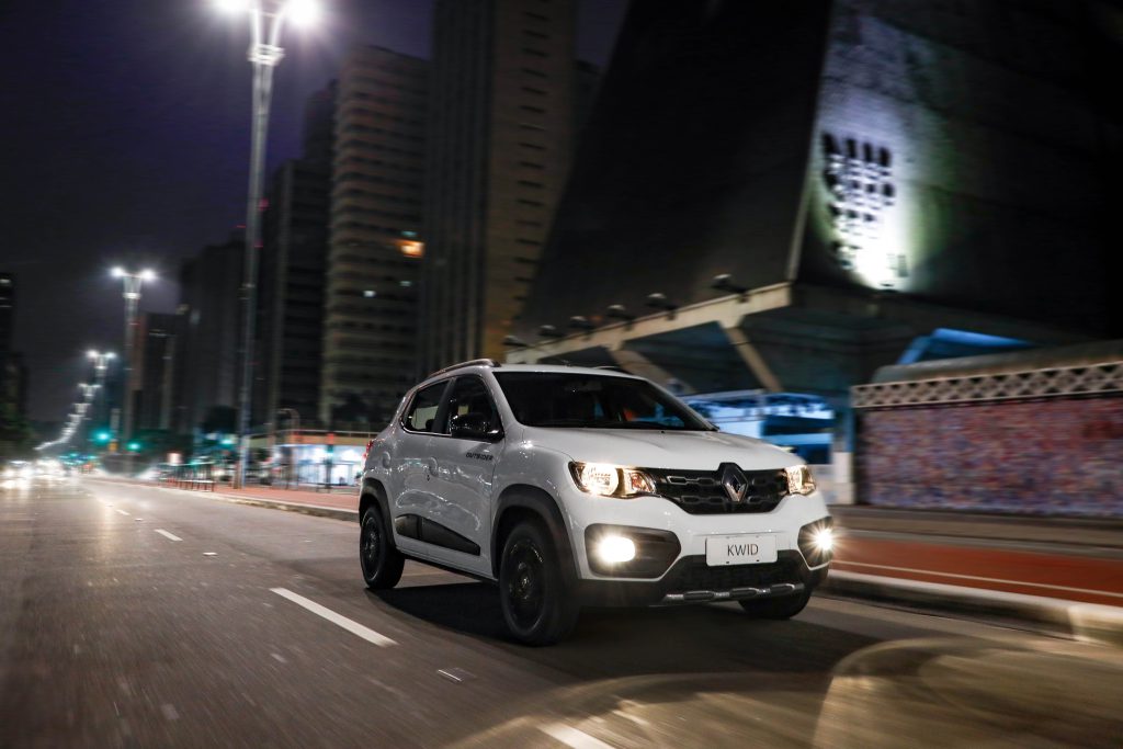 Renault Kwid Outsider branco rodando em estrada urbana, com estilo aventureiro em cenário de cidade.