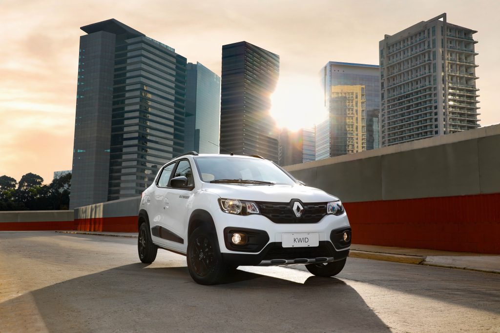 Renault Kwid branco na estrada. Ao fundo, prédios altos com o sol em destaque entre eles.