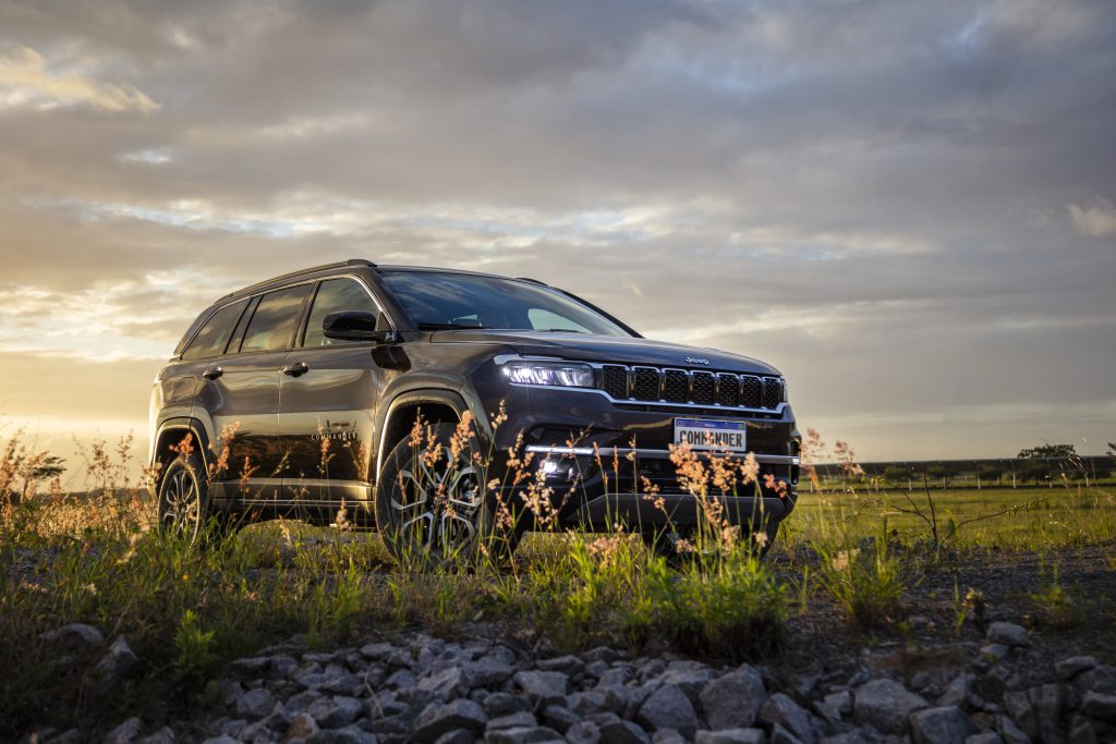 Jeep Commander azul escuro visto de frente em ambiente bucólico, com flores e vegetação ao redor.