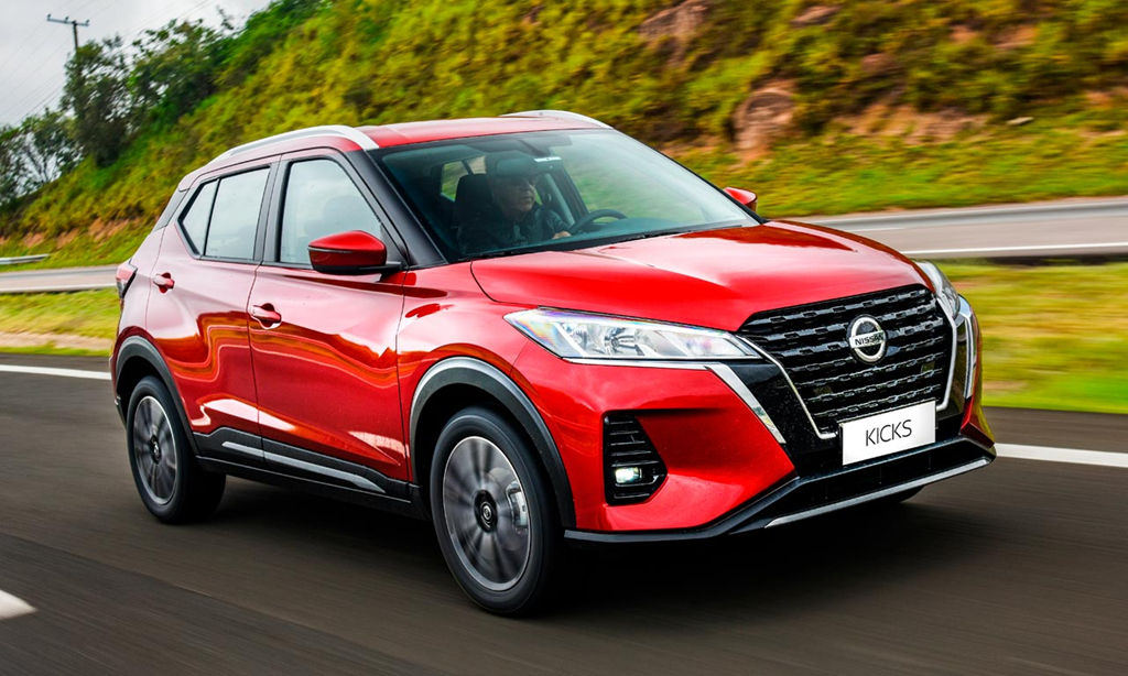 Nissan Kicks vermelho em movimento, com motorista de óculos escuros visível ao volante.