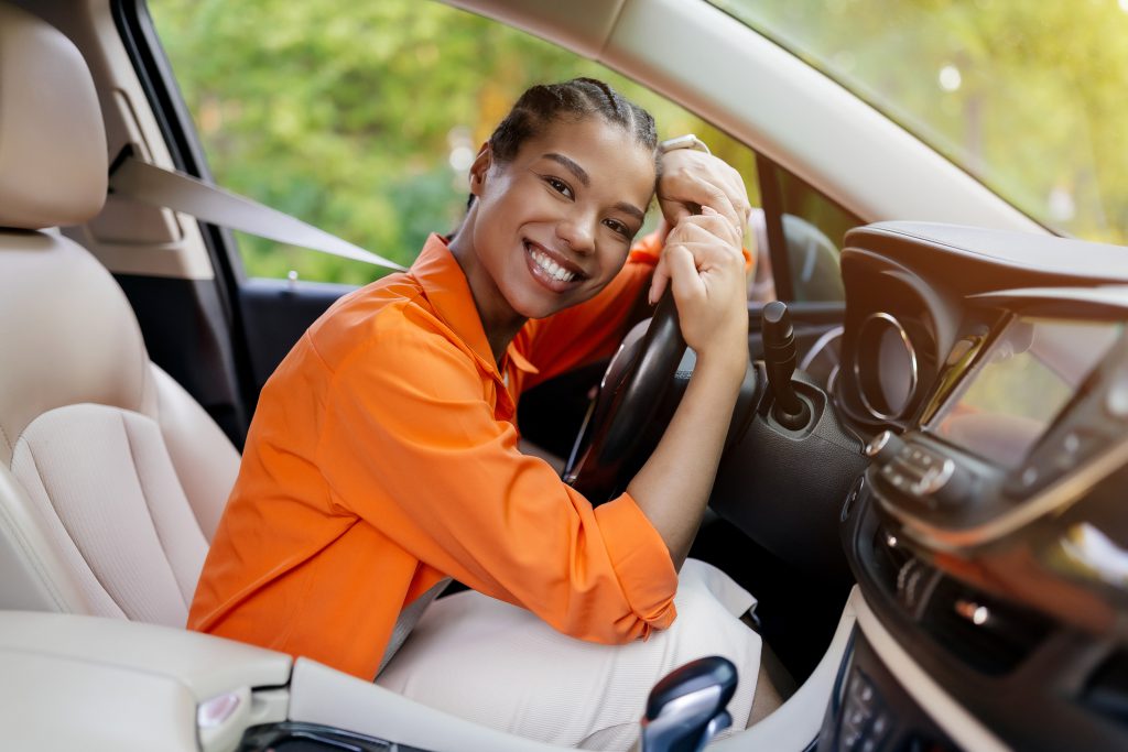 Mulher sorridente abraçada ao volante, transmitindo felicidade por conquistar seu carro.