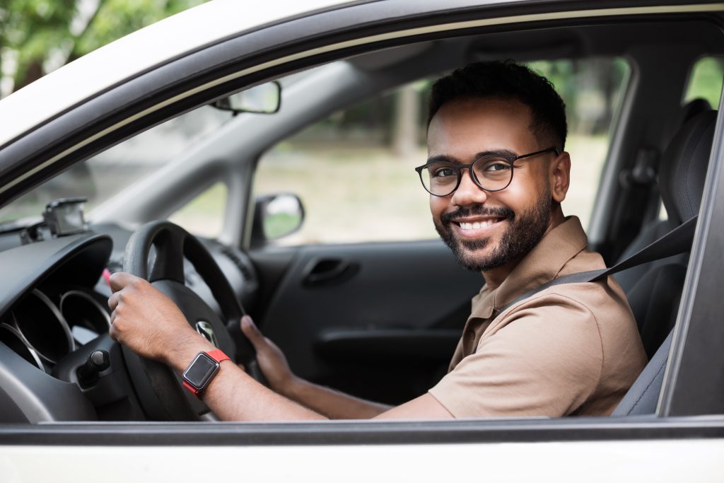 homem sorrindo ao volante, feliz após conquistar seu carro seminovo com financiamento aprovado.